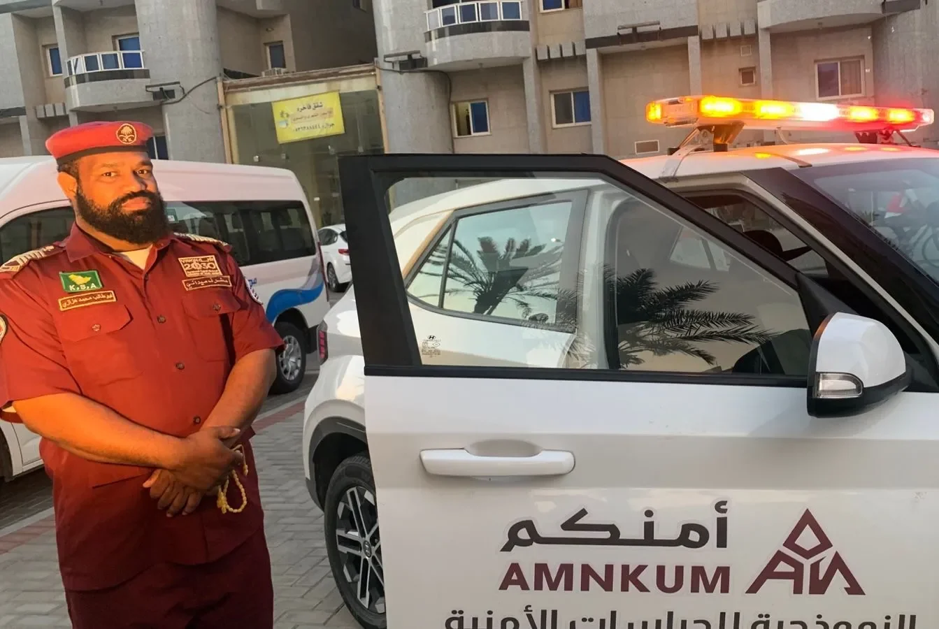 مشرف أمن بجوار سيارة دورية مضاءة